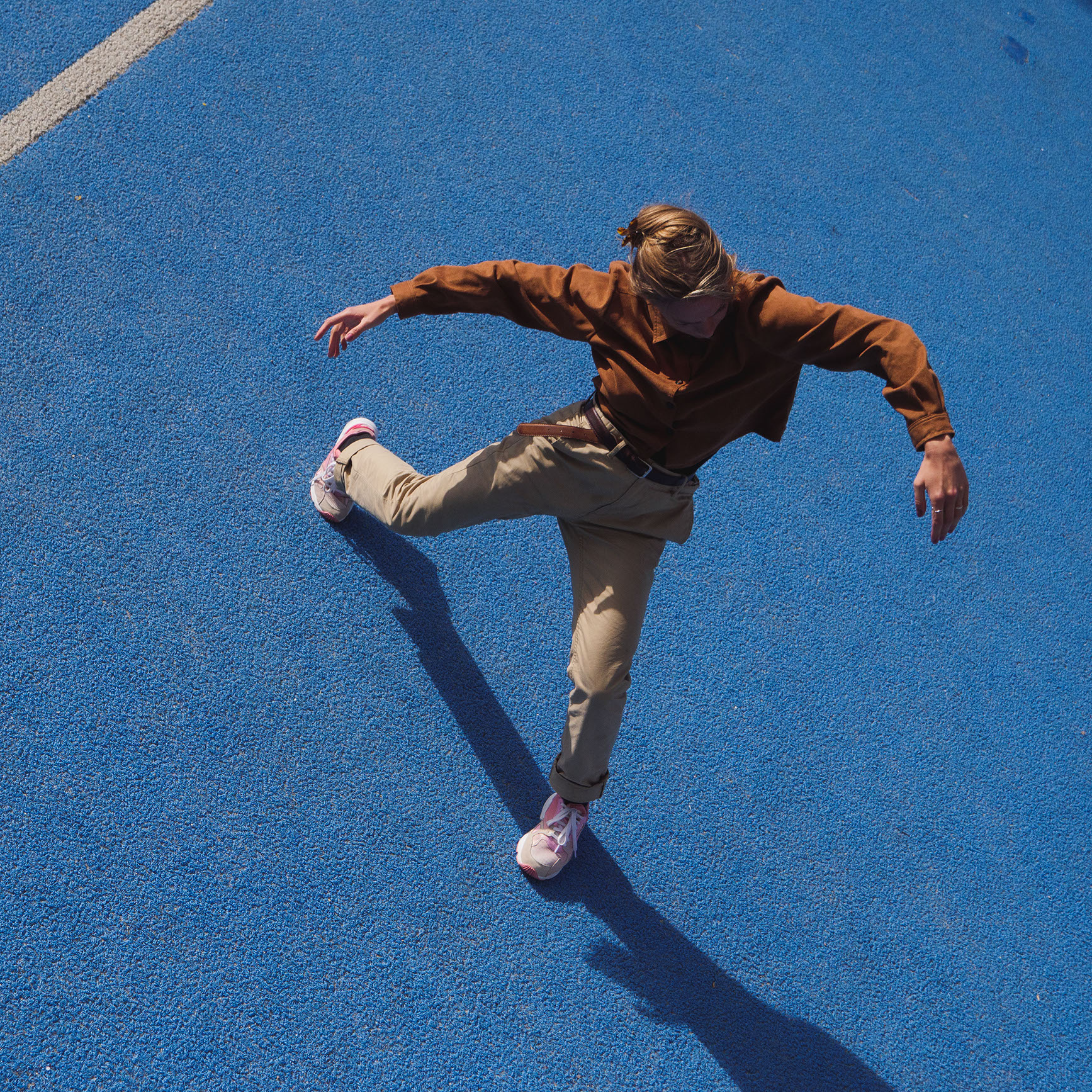 Camilla Schnack Tellefsen dancing on blue ground with brown jacket seen from above
